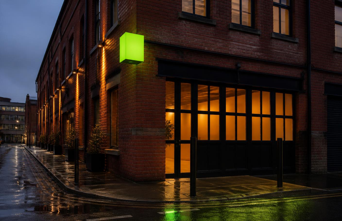 Red brick warehouse building with tall industrial windows lit from inside at dusk